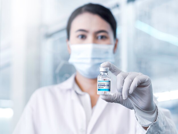 실험실에서 장갑을 끼고 여성 의사 손으로 보여주는 병 유리 병에 현대 라벨 Covid19 백신