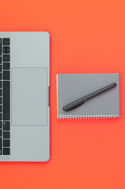 Фото Современный ноутбук и блокнот с ручкой, изолированные на красной поверхности