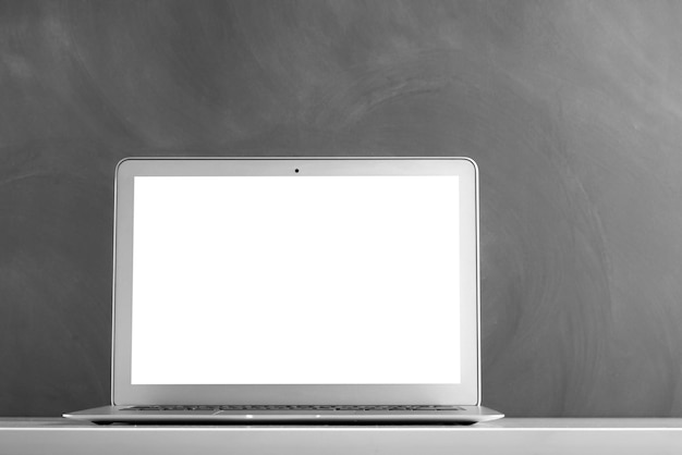 Modern laptop computer on the tabl on the blackboard background