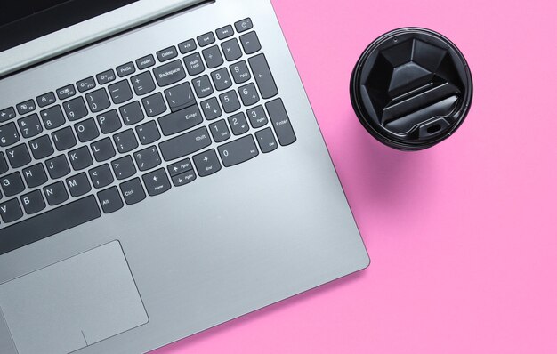 Modern laptop, cup of coffee on pink pastel background. Top view. Office flat lay