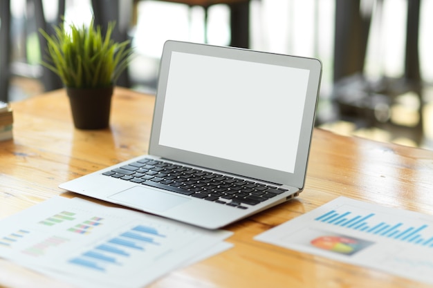 Modern laptop empty screen mockup on wooden worktable with financial report, business workspace, accountant desk