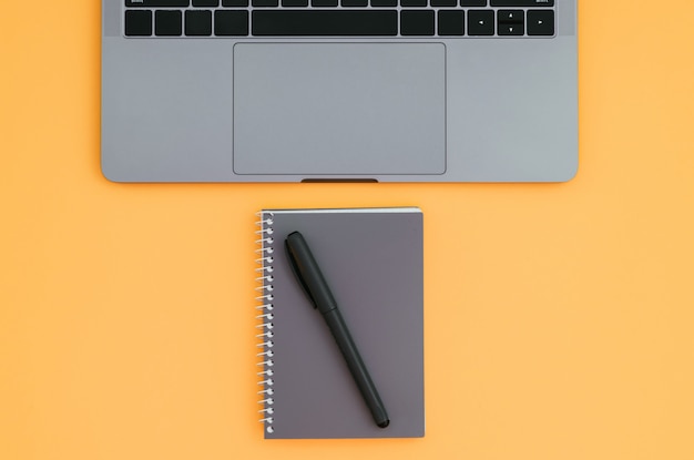 Modern laptop and notepad with a pen isolated on a orange surface