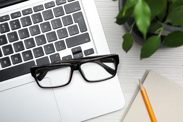 Modern laptop pencil glasses and houseplant on white wooden table flat lay