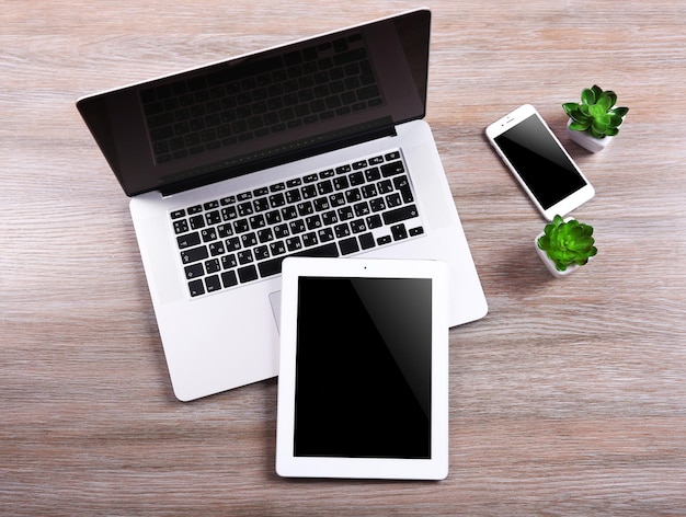 照片现代笔记本电脑智能手机和平板电脑小木桌上绿色植物