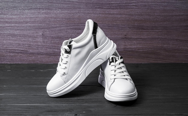 Modern leather white sneakers with laces on wooden background