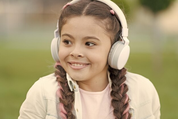 Photo modern lifestyle small child enjoy listening to modern music outdoor little girl wearing modern stereo headphones in summer using modern technology for pleasure and education