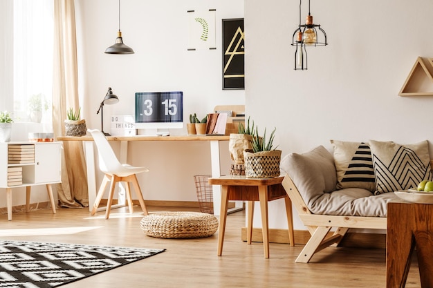 Modern loft-interieur vol natuurlijk houten meubilair en accessoires met bureaucomputer, witte kist, beige slaapbank en papieren potten voor planten