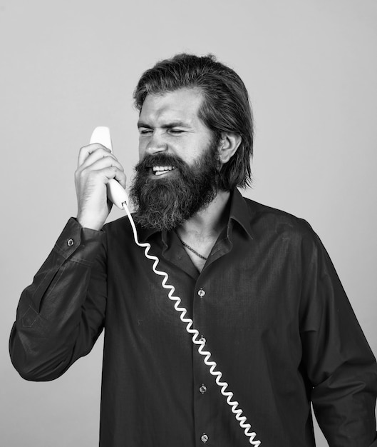 Modern looking bearded hipster speaking on phone communication concept brutal handsome man with moustache use vintage phone mature manager or assistant conversation Be Direct