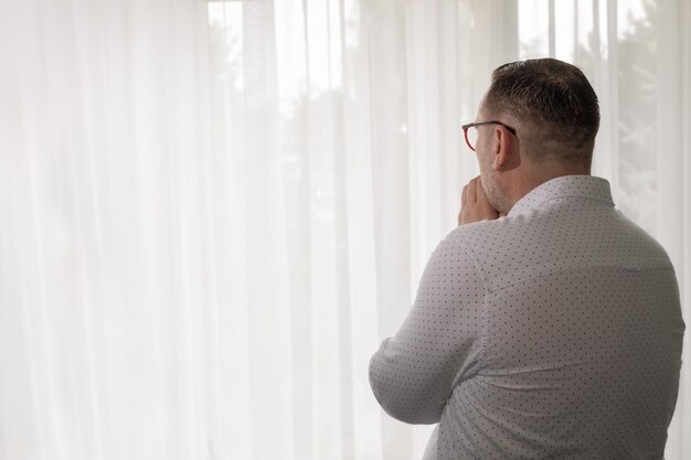 A modern man mourns while standing at the window