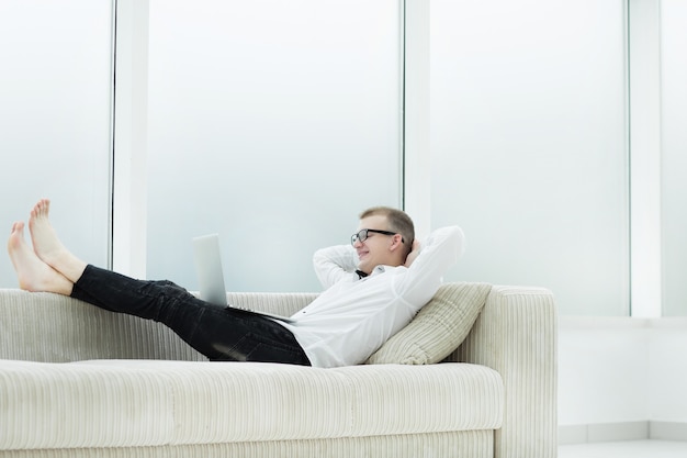 Modern man with laptop lying on sofa in living room. photo with copy space