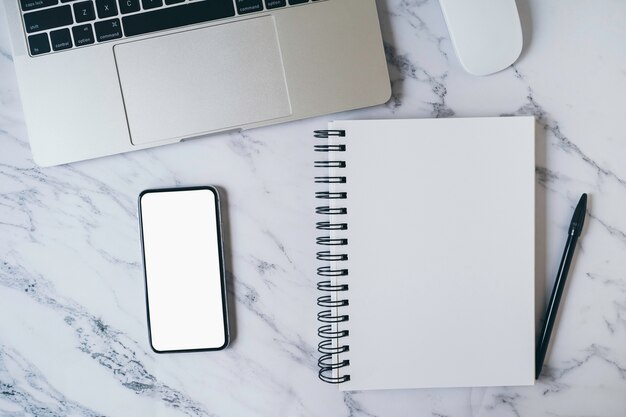 Modern marble office desk table with laptop, blank white mobile phone screen and notebook page for input text or entry short note, copy space for creative content and design. Top view, flat lay