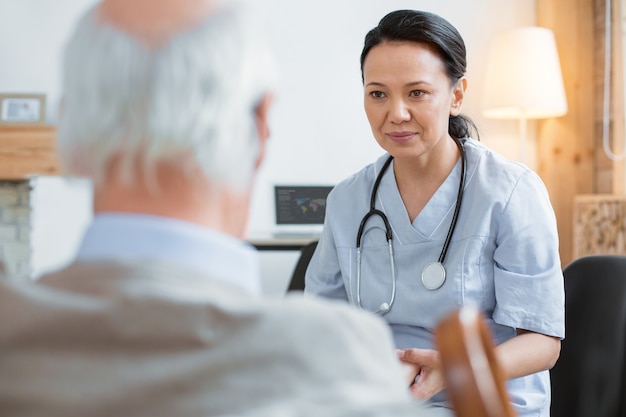 Modern medicine. Concentrated asian doctor staring at senior man while wearing uniform and sitting