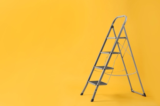 Modern metal stepladder on yellow background Space for text