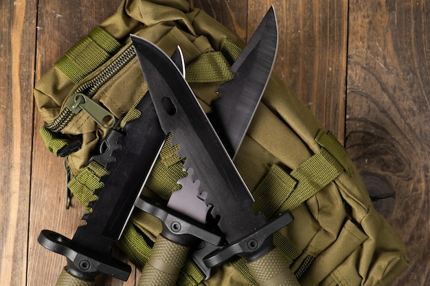 현대적인 군용 칼과 그것을 위한 플라스틱 칼집 가장자리가 있는 무기는 군용 올리브색 배낭에 놓여 있습니다