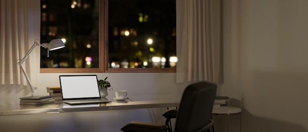 Современное минимальное домашнее рабочее пространство ночью с макетом ноутбука на столе у окна