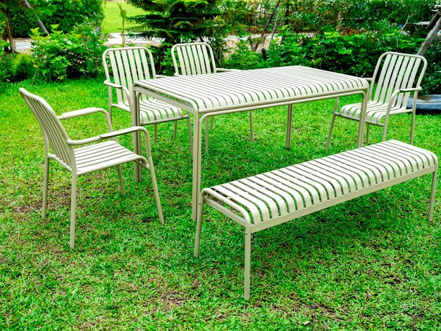 現代的なミニマルテーブルセット テーブル ベンチとアームチェア 座席 ストライプ パターン ベージュ色 緑の草の上の鉄の材料 屋外の庭の庭園の風景 背景 人がいない