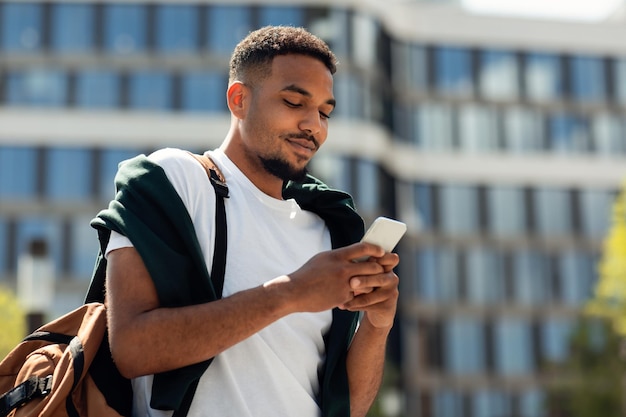 都市を屋外で歩くスマートフォンを使用して黒のスタイリッシュな男の現代のモバイル通信の肖像画