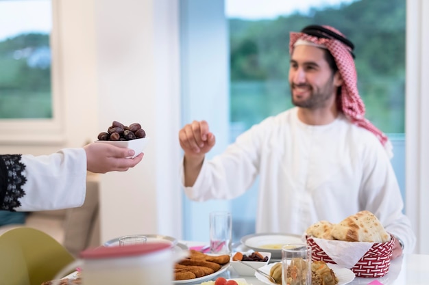 現代の多民族のイスラム教徒の家族が、自宅でラマダンの饗宴の間にイフタールディナーを楽しみながら、デートのボウルを共有しています。
