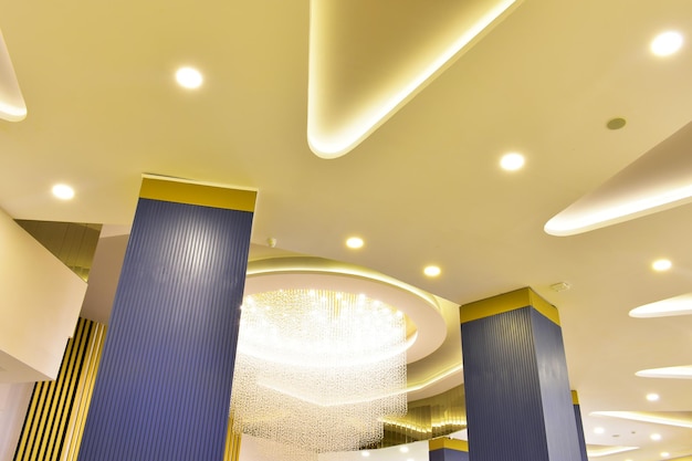 Modern multilevel beige ceiling with hanging luminous threads and blue columns