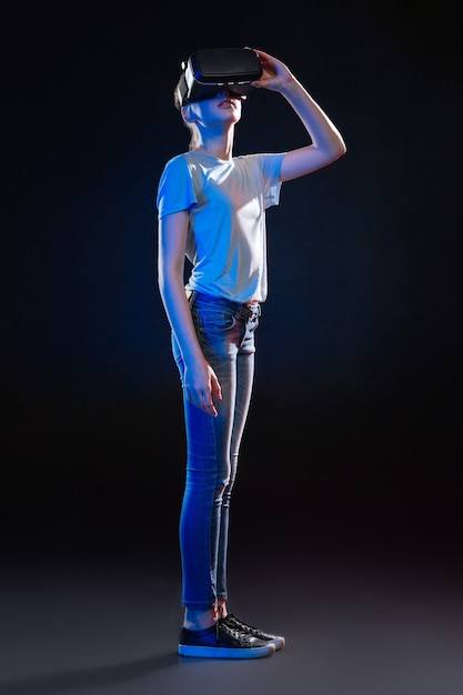 Modern multimedia. Pleasant cute woman using VR glasses while standing against black background