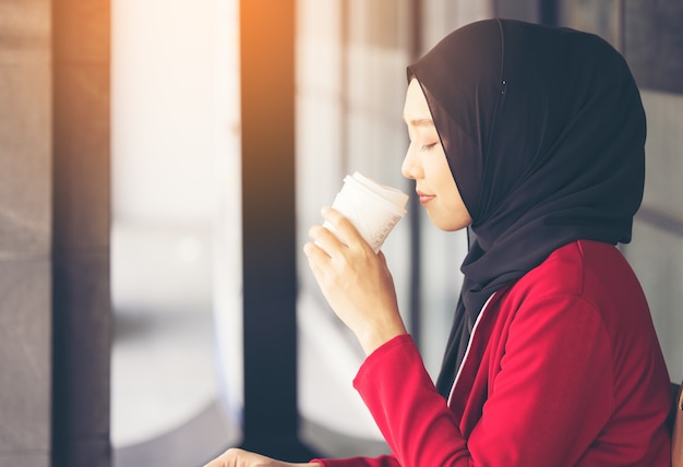 持ち帰り用のコーヒーを飲みながら通りを歩いている現代のイスラム教徒の女性