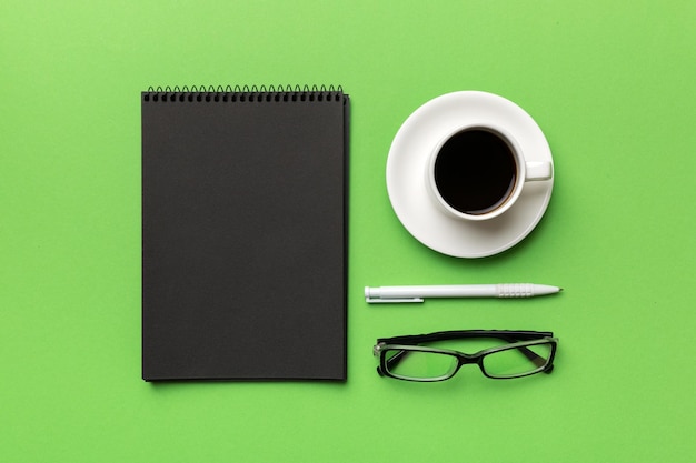 ノートブックとコーヒーのカップと他の物資を備えたモダンなオフィスデスクテーブルあなたのための空白のノートブックページデザイントップビューフラットレイ