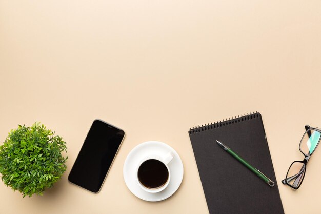 Современный офисный стол с ноутбуком, смартфоном и другими принадлежностями с чашкой кофе. Пустая страница блокнота для вашего дизайна. Вид сверху на плоскую планировку.
