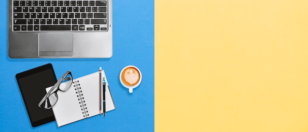 Foto posto di lavoro da tavolino dell'ufficio moderno con lo spazio della copia su fondo giallo e blu luminoso