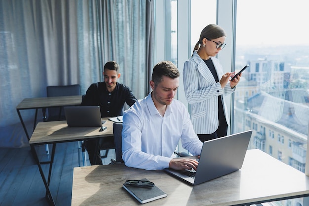 Modern office young team of businessmen in formal wear\
discussing project details and looking at laptop screen while\
collaborating during meeting in modern boardroom