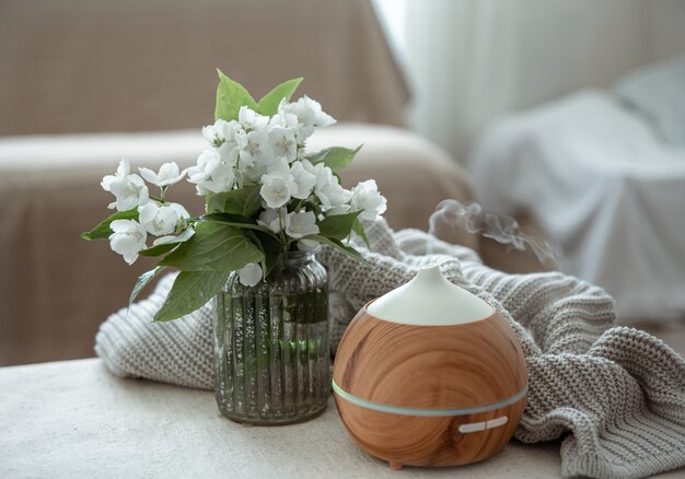 Modern oil aroma diffuser in the living room on the table with knitted element and flowers.