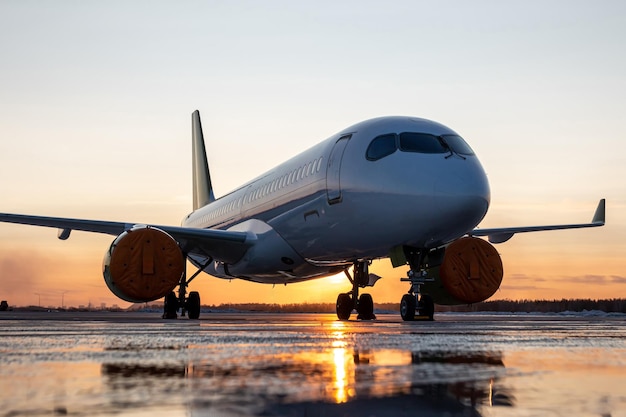 Modern passenger airplane on the airport apron against the backdrop of a picturesque sunset