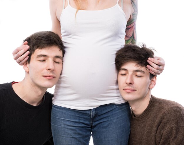 Modern polygamous family with one wife  and two husbands. Young pregnant woman posing with two young man on a white background