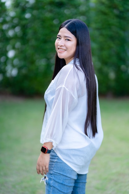 Modern portret van een mooie, gelukkige Aziatische vrouw die een smartwatch draagt en een mooie witte jurk draagt en een jeanslevensstijl draagt die geniet van de grasachtergrond