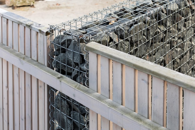 Modern privacy fence made of wood boards and gabion galvanized steel grid with granite stones