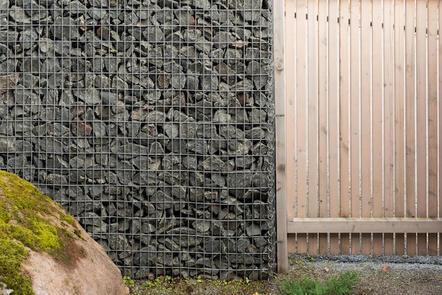 Modern privacy fence made of wood boards and gabion galvanized steel grid with granite stones