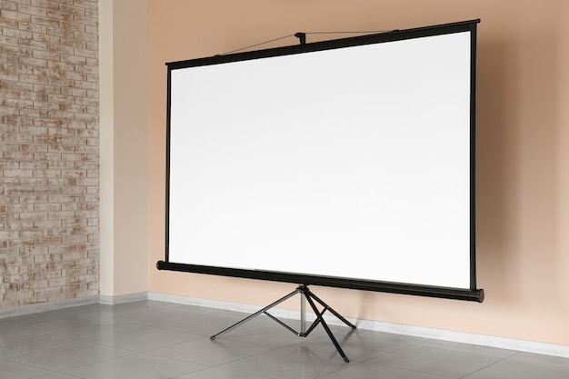 Modern projector screen near wall indoors