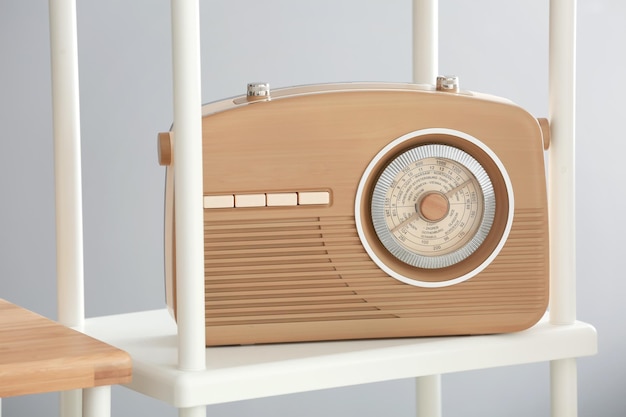 Modern radio receiver on shelf against light background