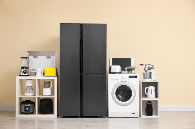 Modern refrigerator and other household appliances near beige wall indoors