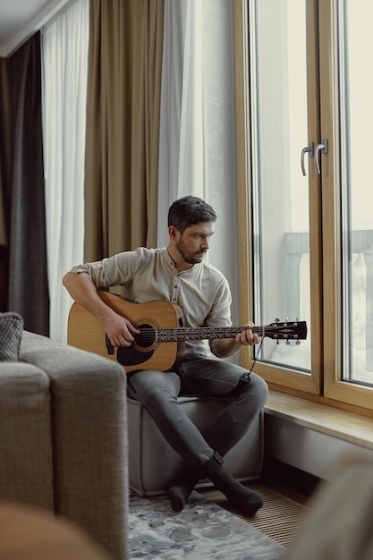 현대의 낭만적인 남자 음악가는 어쿠스틱 기타를 연주하고 잘생긴 기타 연주자는 집에서 여가 시간을 보낸다