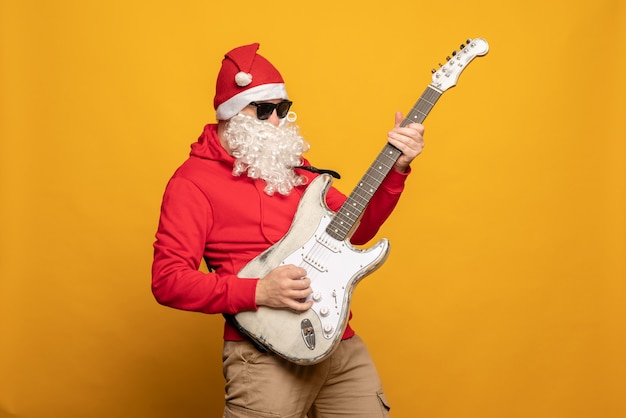 현대 산타 클로스 락 앤 롤러는 노란색 배경에 감정적으로 고립된 기타를 연주합니다.