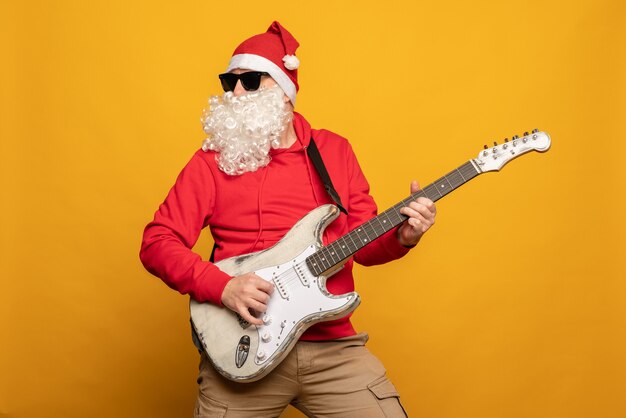 Il moderno babbo natale rock n roller suona la chitarra emotivamente isolato su sfondo giallo