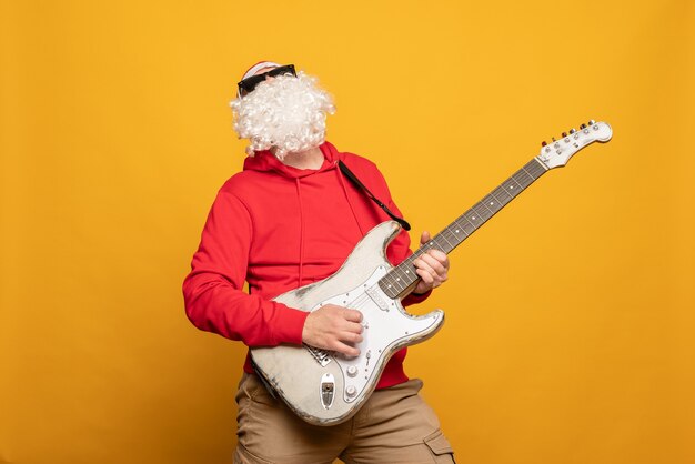 Modern santa claus rock n roller play guitar emotionally\
isolated on yellow background