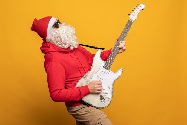 Modern santa claus rock n roller play guitar emotionally isolated on yellow background