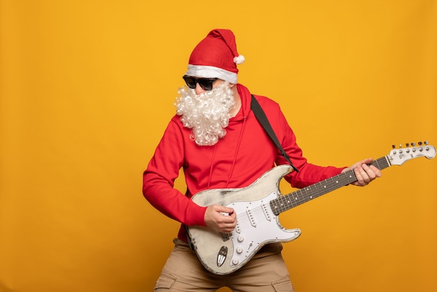 현대 산타 클로스 락 앤 롤러는 노란색 배경에 감정적으로 고립된 기타를 연주합니다.