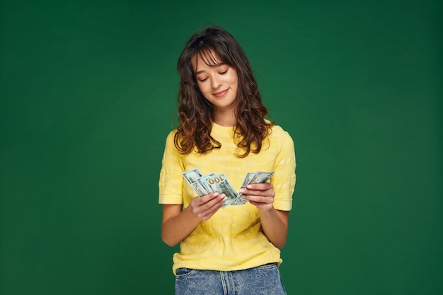 Modern satisfied young girl count cash money on green studio background financial fortune success