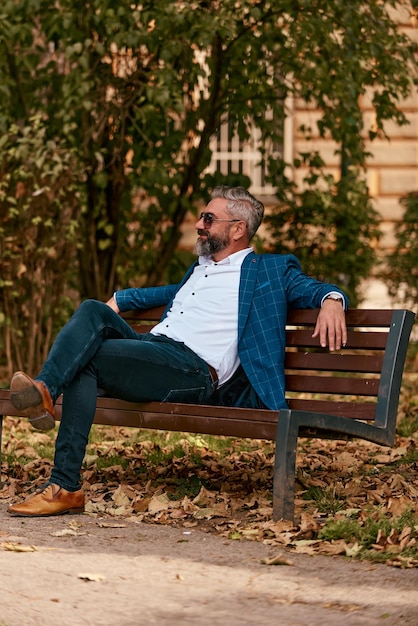 Современный старший бизнесмен отдыхает на скамейке в городе в перерыве от работы.