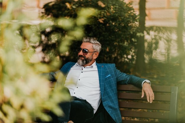 Foto moderno uomo d'affari senior che riposa su una panchina in città in una pausa dal lavoro.