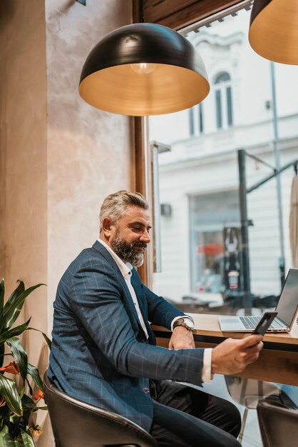 Photo modern senior businessman sitting in cafe and using laptop and smartphone