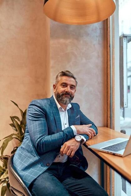 Photo modern senior businessman sitting in cafe and using laptop and smartphone.