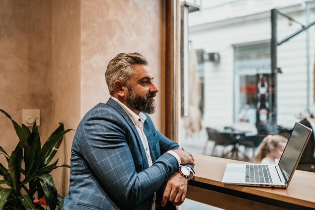 Modern senior businessman sitting in cafe and using laptop and smartphone.